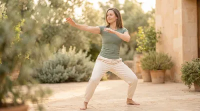 Woman in sage green performing tai chi single whip in a minimalist courtyard at dawn