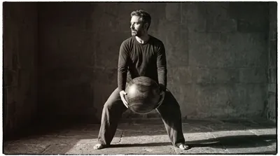 Practitioner holding a large wooden ball at the abdomen in dramatic warm side lighting