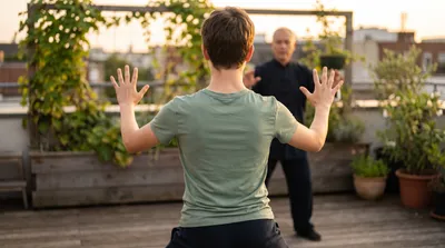 Teenager practising a tai chi posture at golden hour on a rooftop garden with an instructor behind