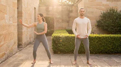 Two practitioners side by side performing tai chi and qigong in a warm courtyard