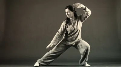 Practitioner holding the White Crane Spreads Its Wings posture with one hand high and one low