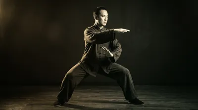 Black and white photograph of a tai chi practitioner performing Yang style brush knee in dramatic side lighting