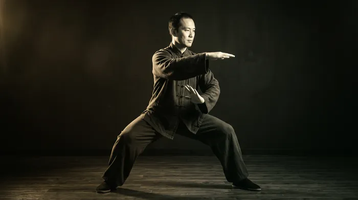 Black and white photograph of a tai chi practitioner performing Yang style brush knee in dramatic side lighting